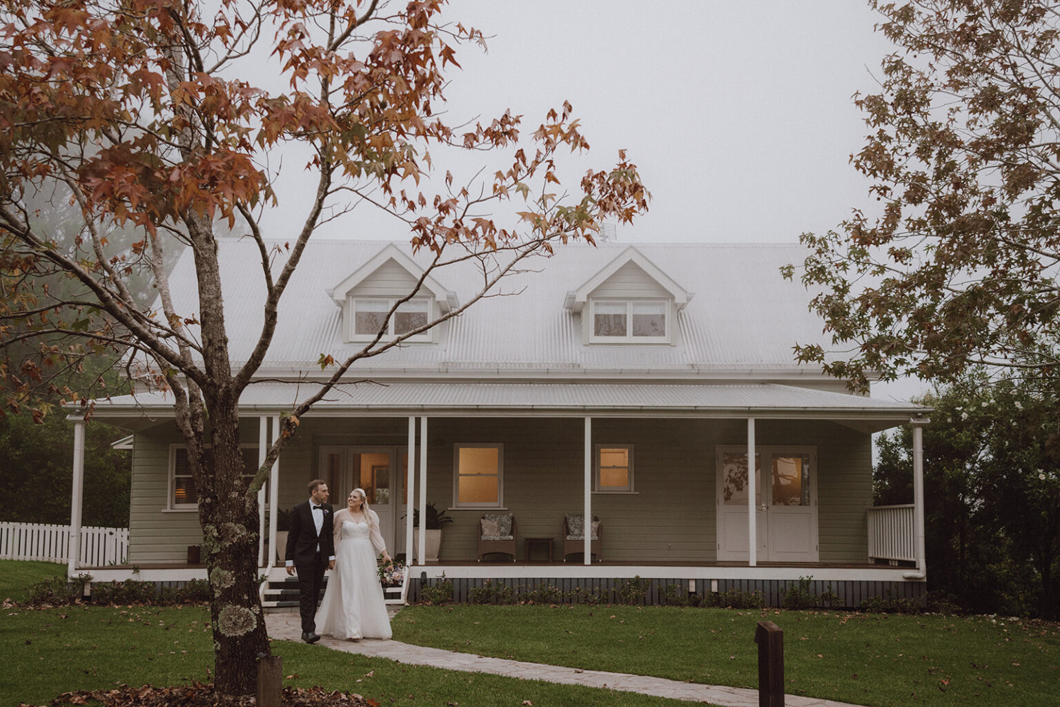 Couple outside the Clovelly homestead framed by autumn leaves