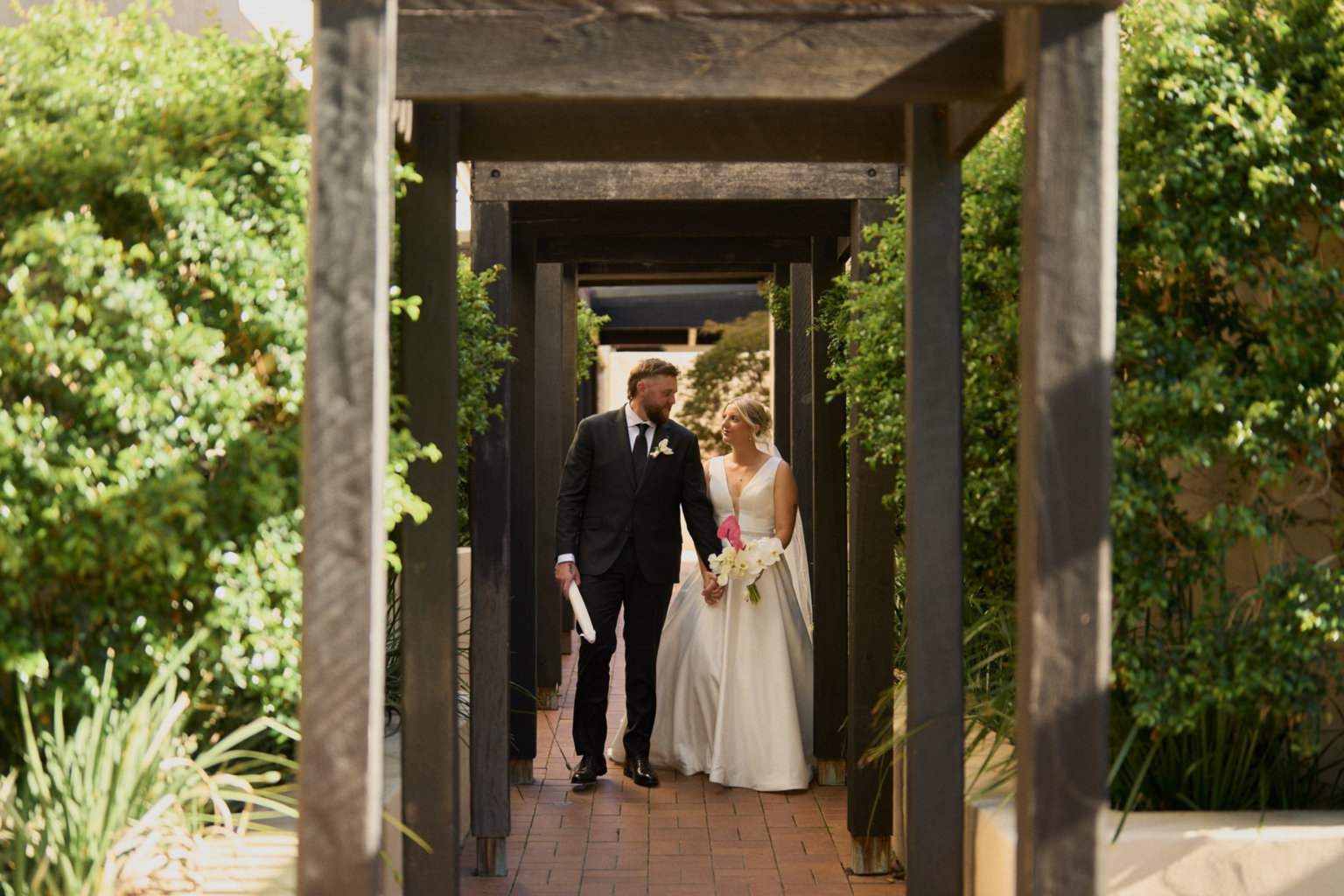 Bride and groom holding hands beneath a timber pergola at Tower Lodge