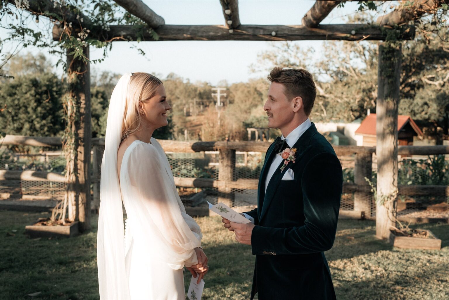 Groom reading his vows to the bride beneath the timber pergola