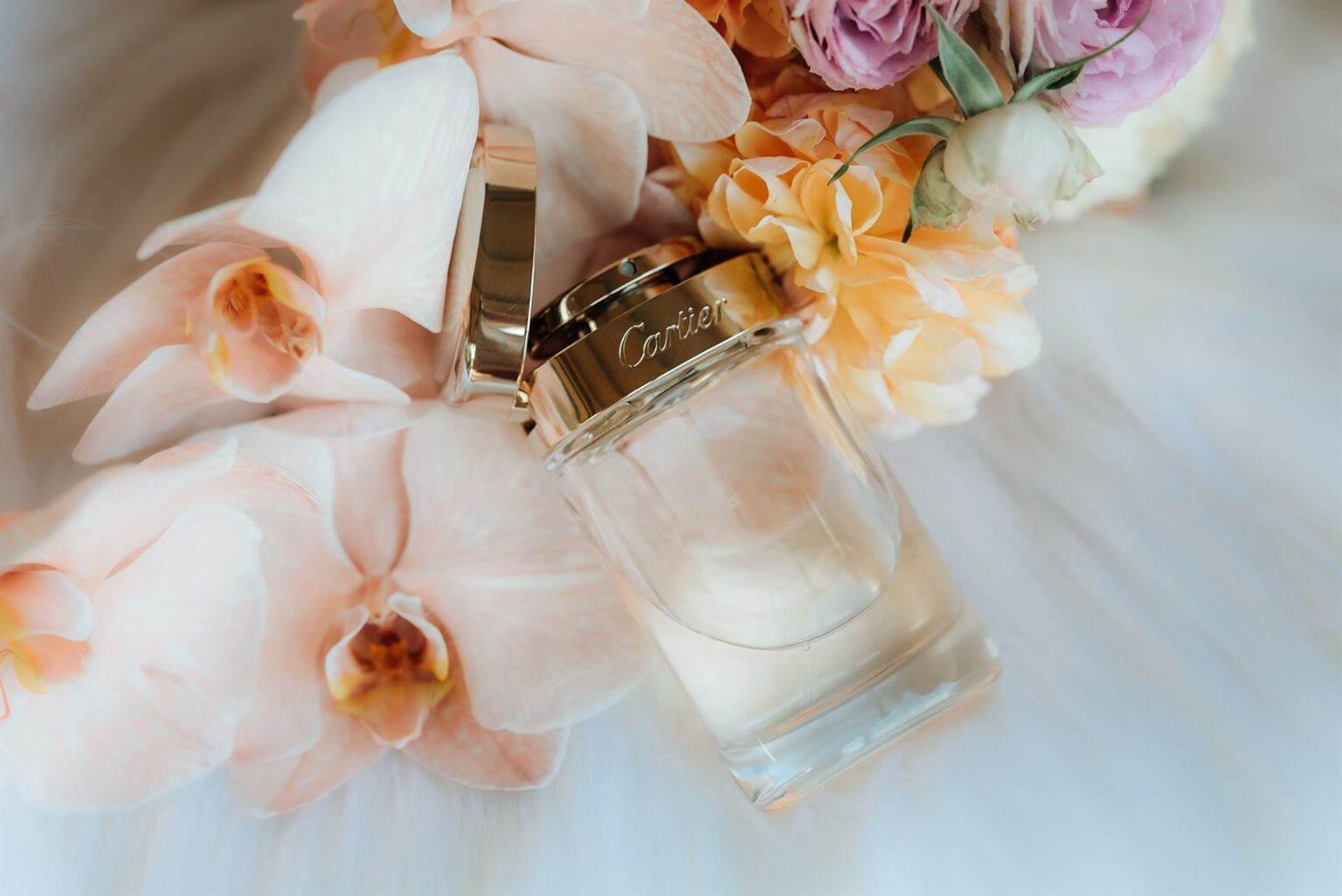 Perfume bottle among peach and blush orchids