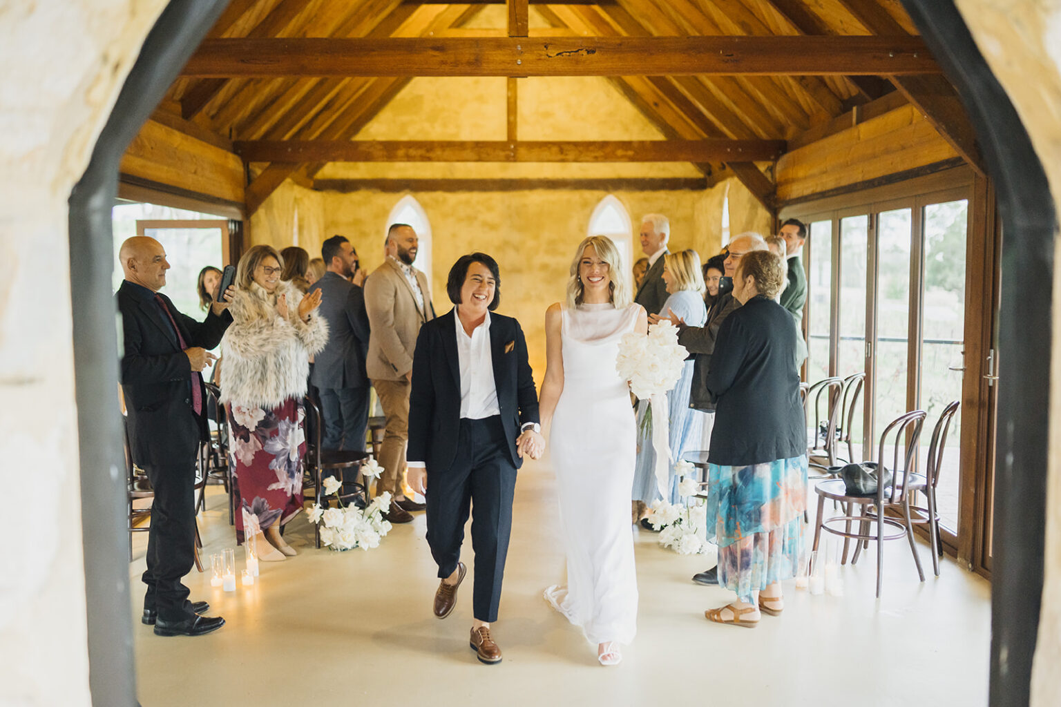 Newlyweds walking back down the chapel aisle as guests cheer