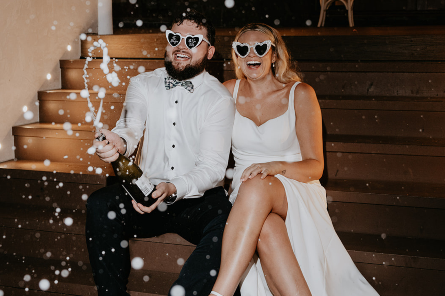 Couple in heart sunglasses popping champagne on the steps