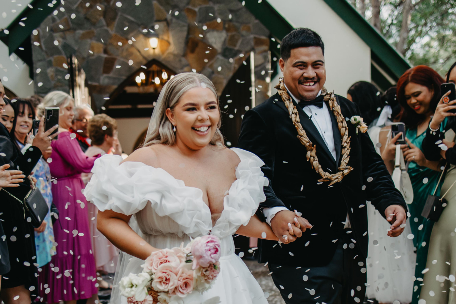 Newlyweds leaving the chapel under confetti with guests cheering