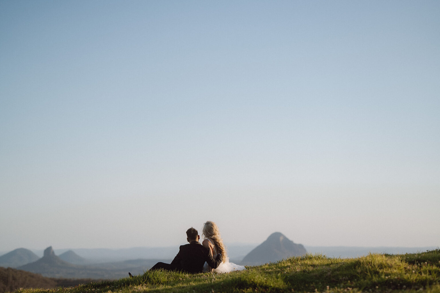 Couple sitting on a hill overlooking the Glass House Mountains