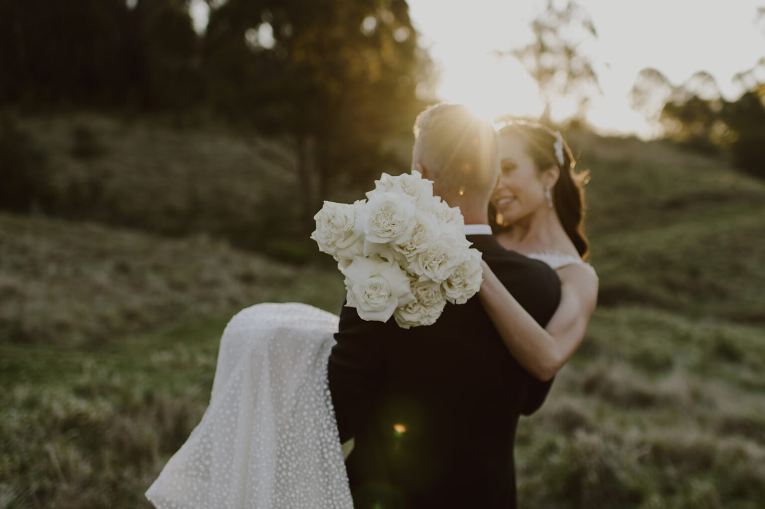 Groom carrying the bride through the grass at golden hour