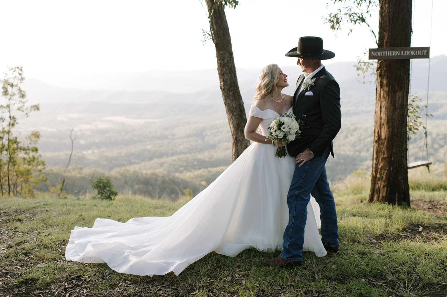 Groom in a cowboy hat embracing the bride at the mountain lookout