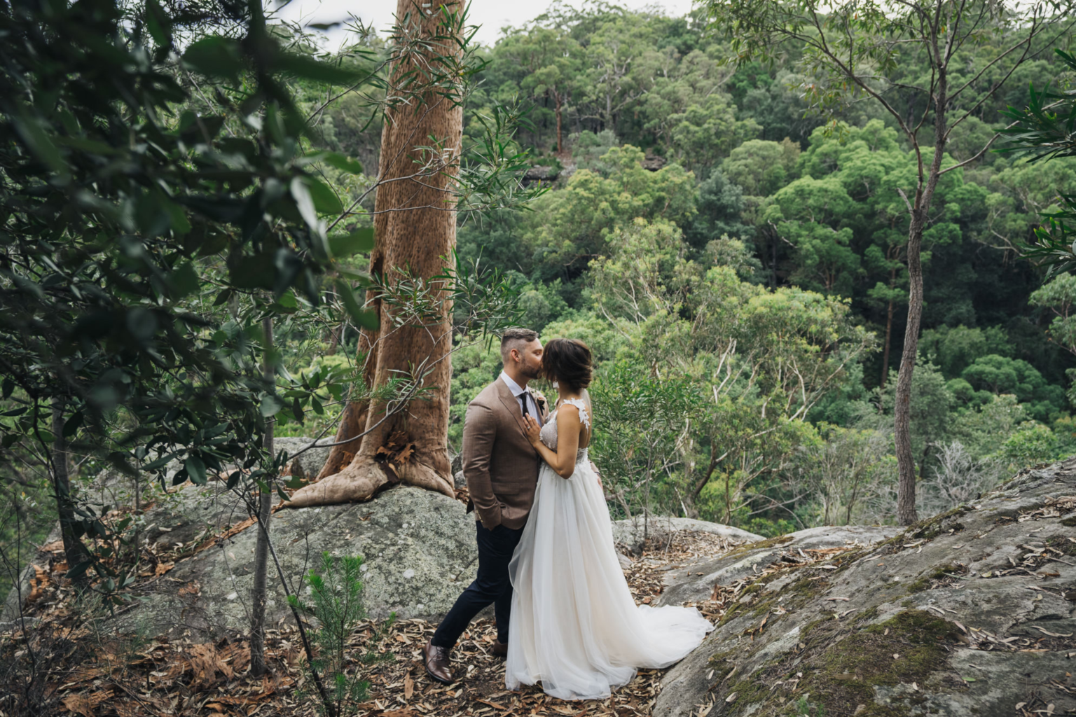 Groom kissing the bride on the rocks overlooking the valley