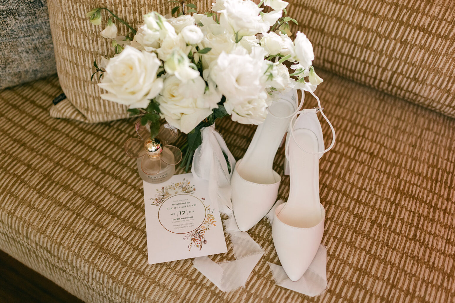 White rose bouquet, bridal shoes and invitation on a woven chair