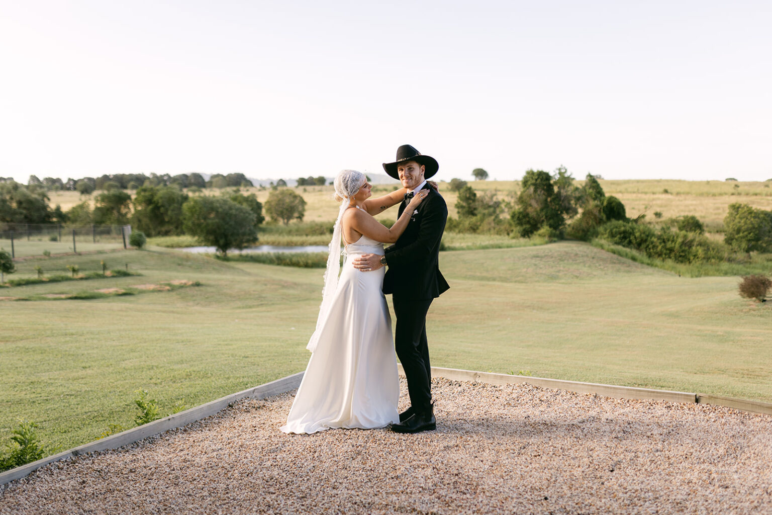 Groom in a cowboy hat embracing the bride on the lawn at Twigley Farm