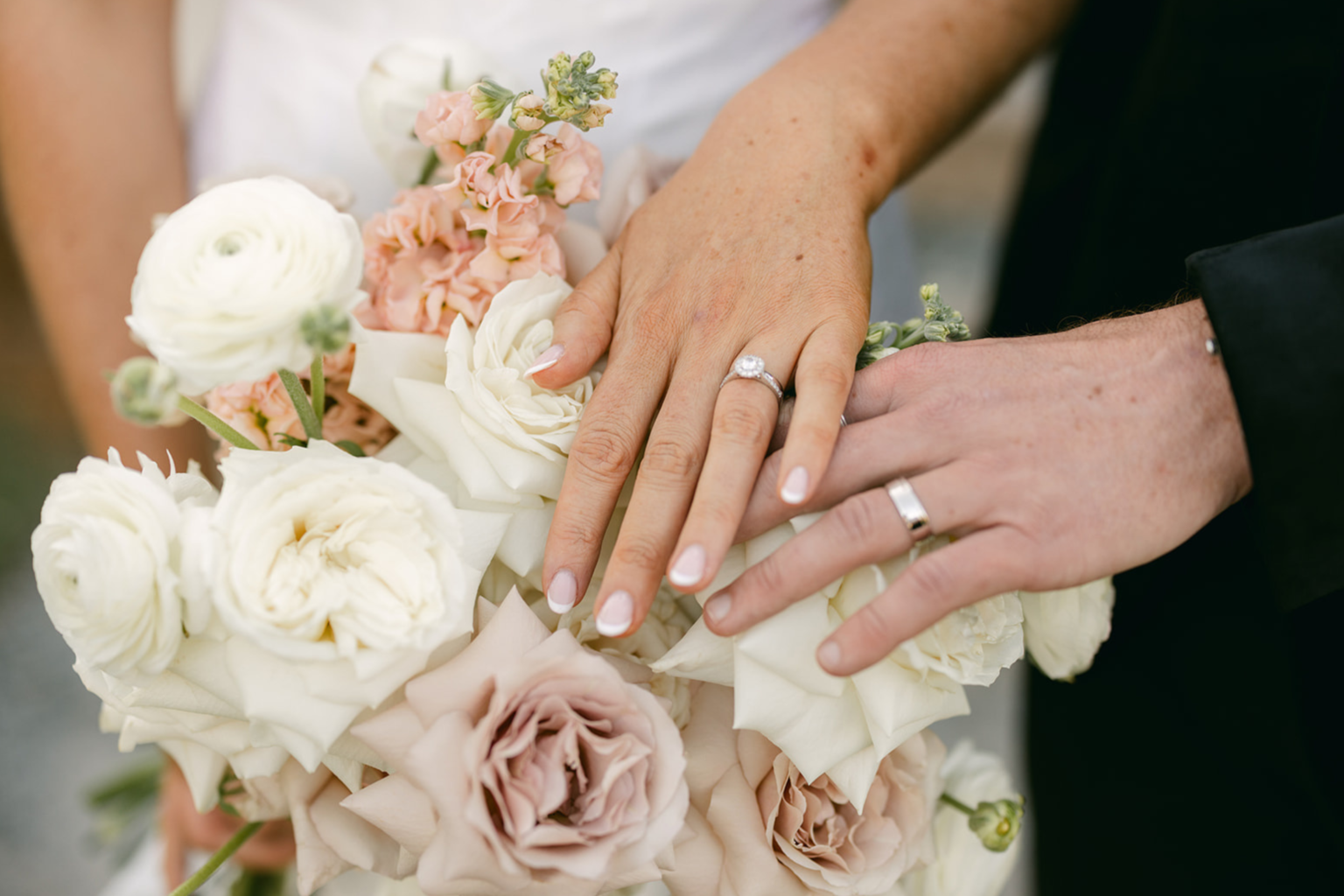 Close-up of the couple's hands and rings on a blush rose bouquet