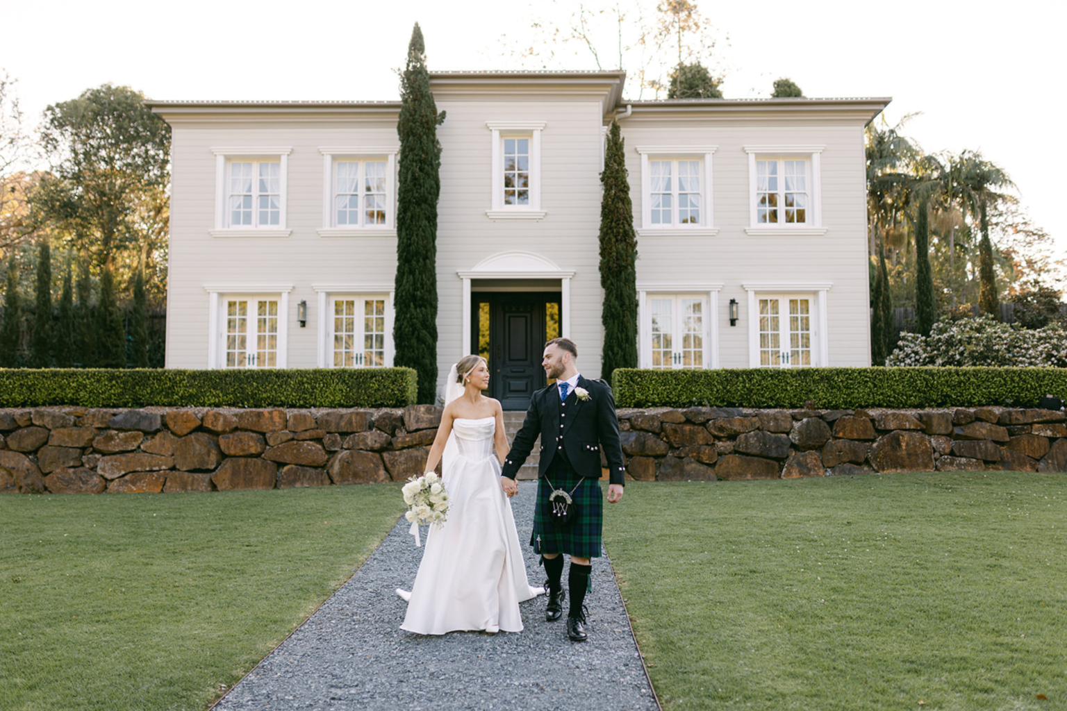 Bride and groom walking from the manor along the garden path