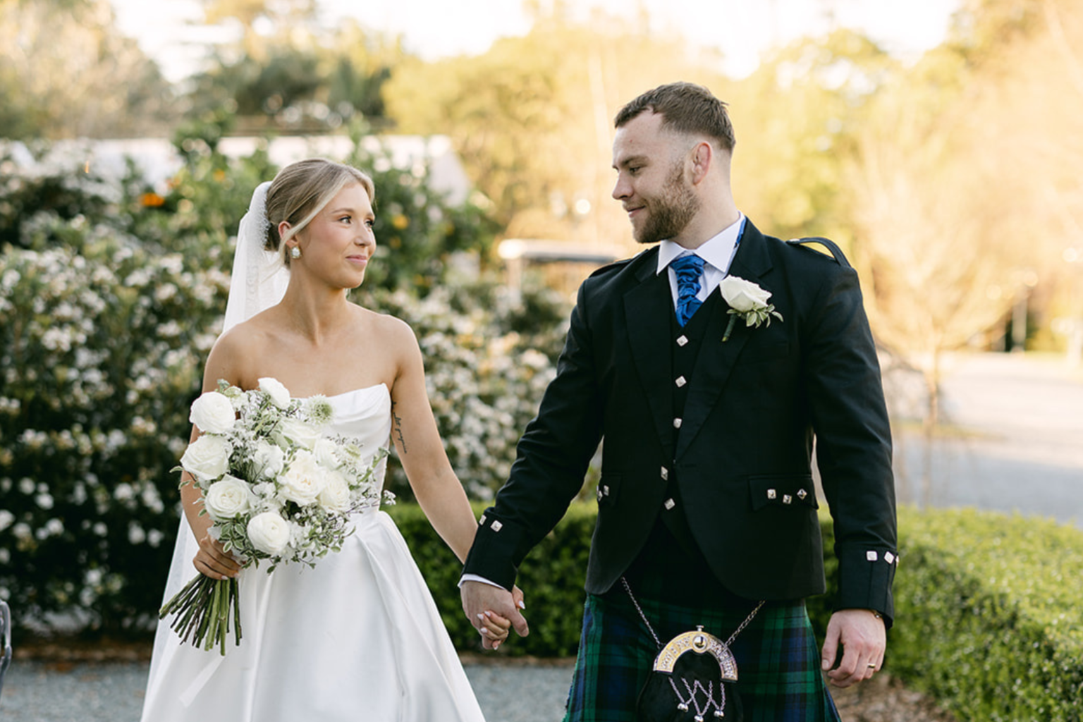 Bride and groom in a kilt holding hands in the gardens