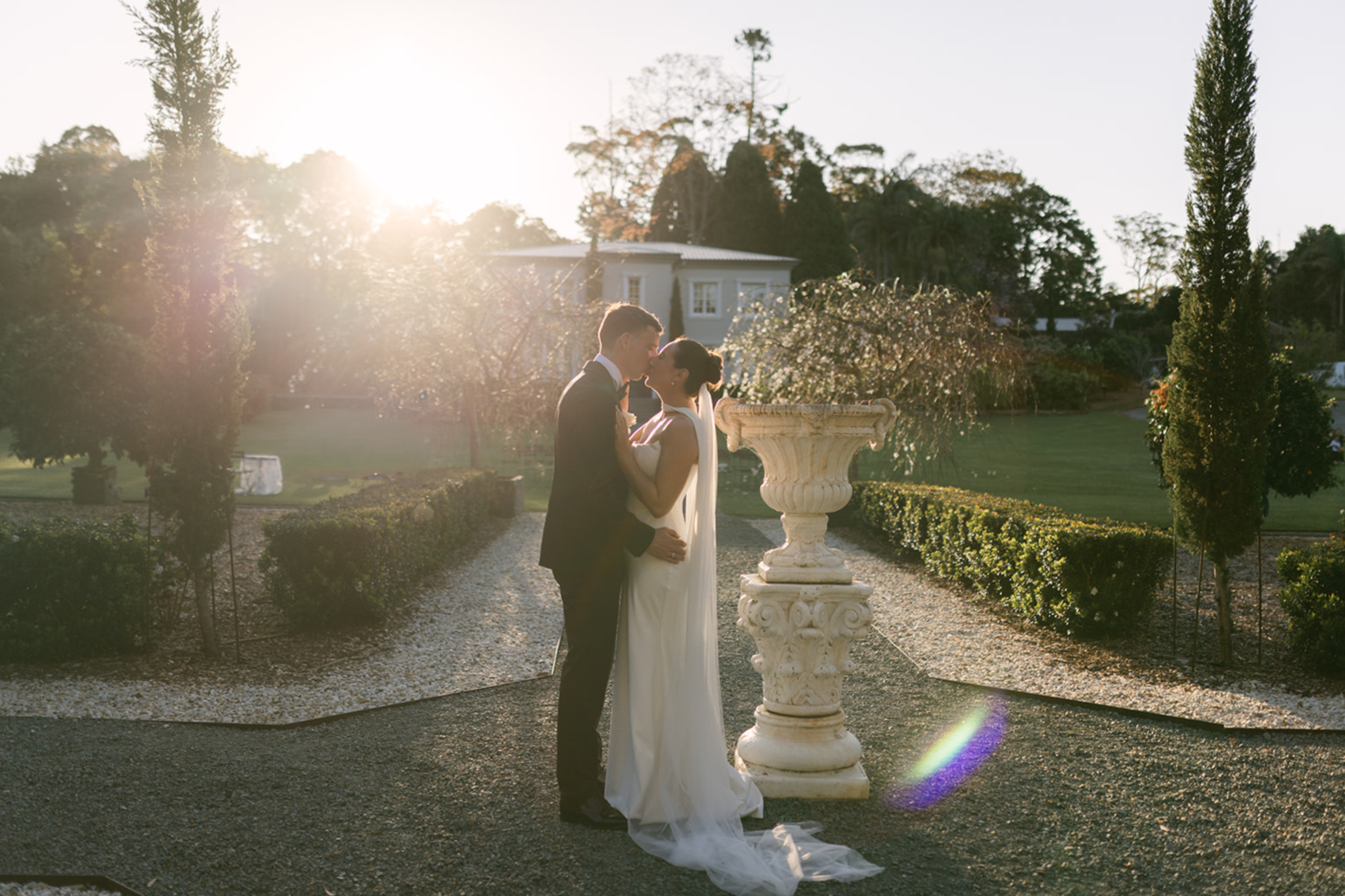 Couple kissing beside a garden urn at sunset
