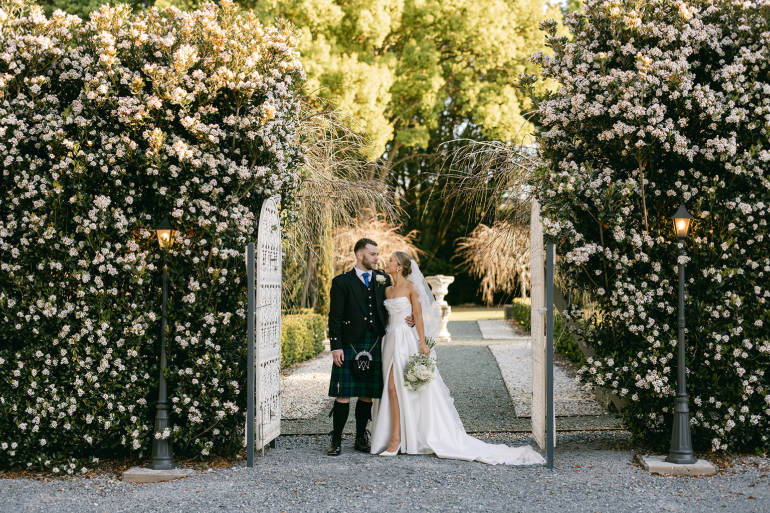 Couple at the garden gate framed by flowering hedges at Wynmère Estate