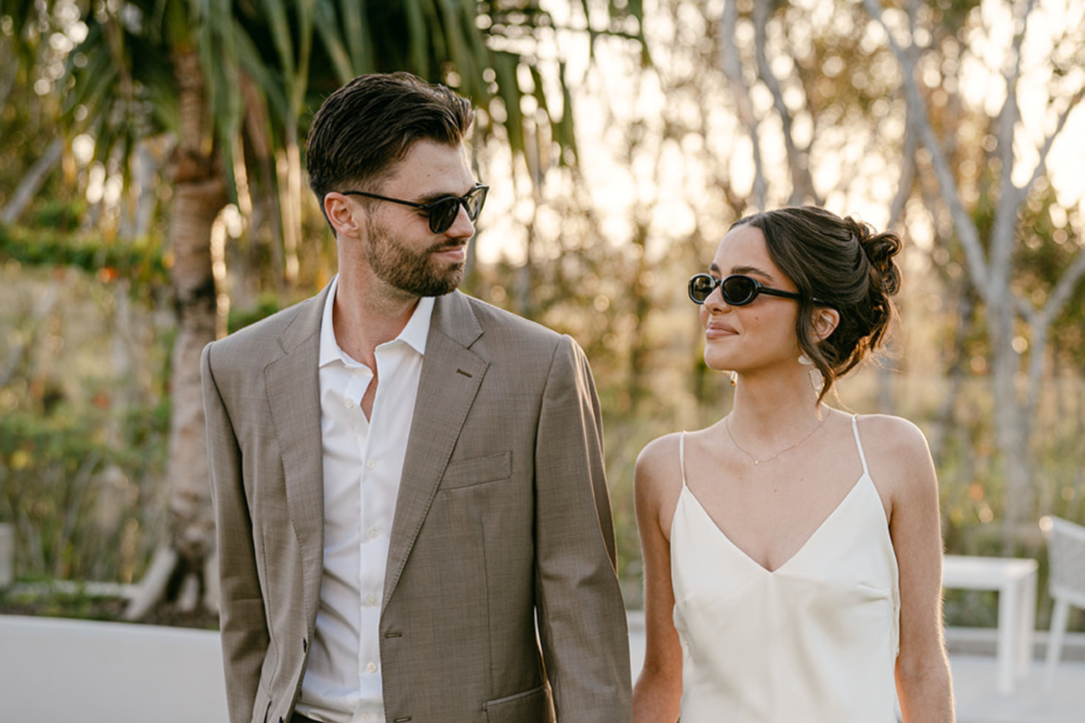 Couple in sunglasses smiling at each other among the palms