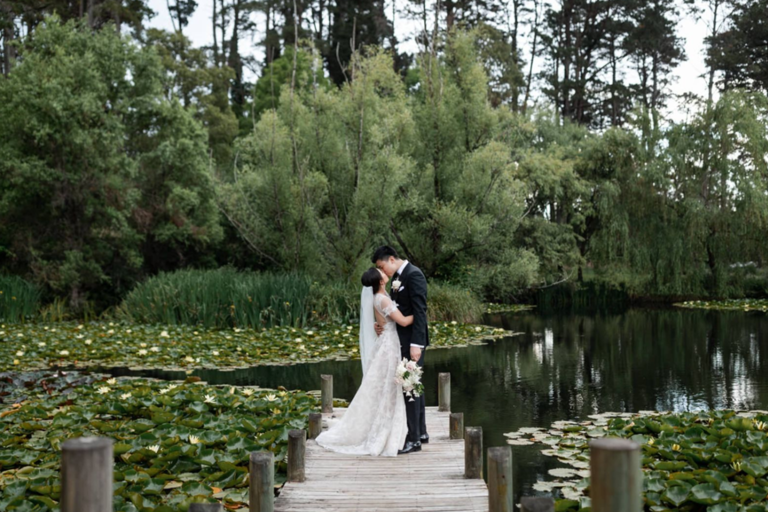 Bride and groom kissing on the lily pond boardwalk at Parklands