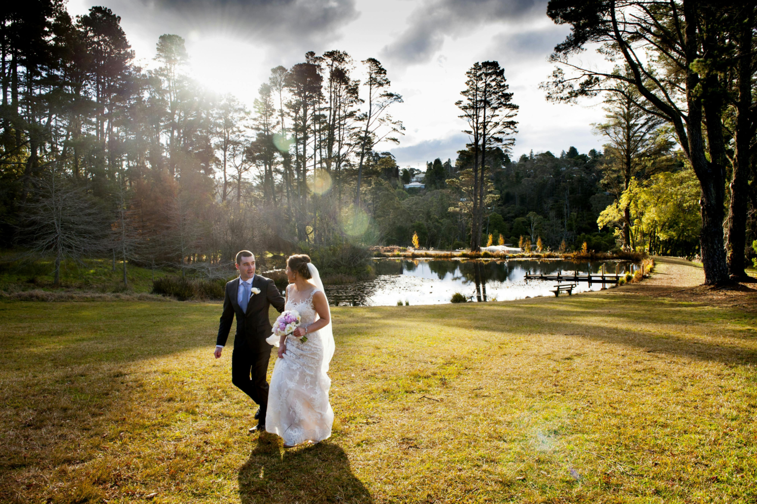Bride and groom walking across the lawn by the lake at Parklands