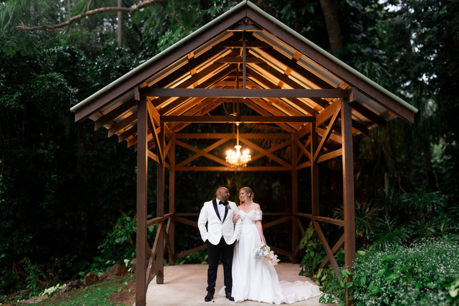 Bride and groom under a lantern-lit timber pavilion at Rainforest Gardens