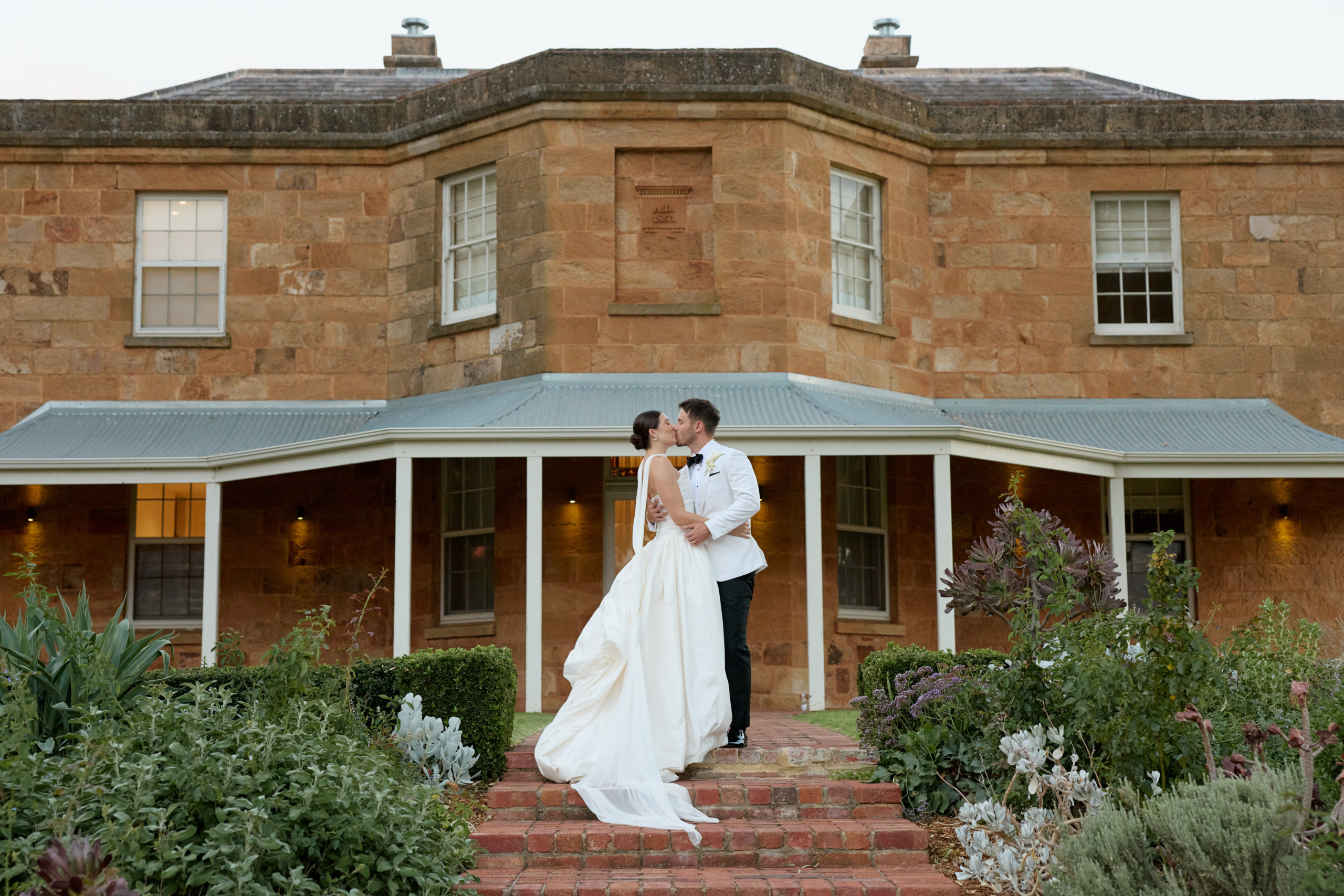 Bride and groom kissing on the steps of the Kingsford homestead