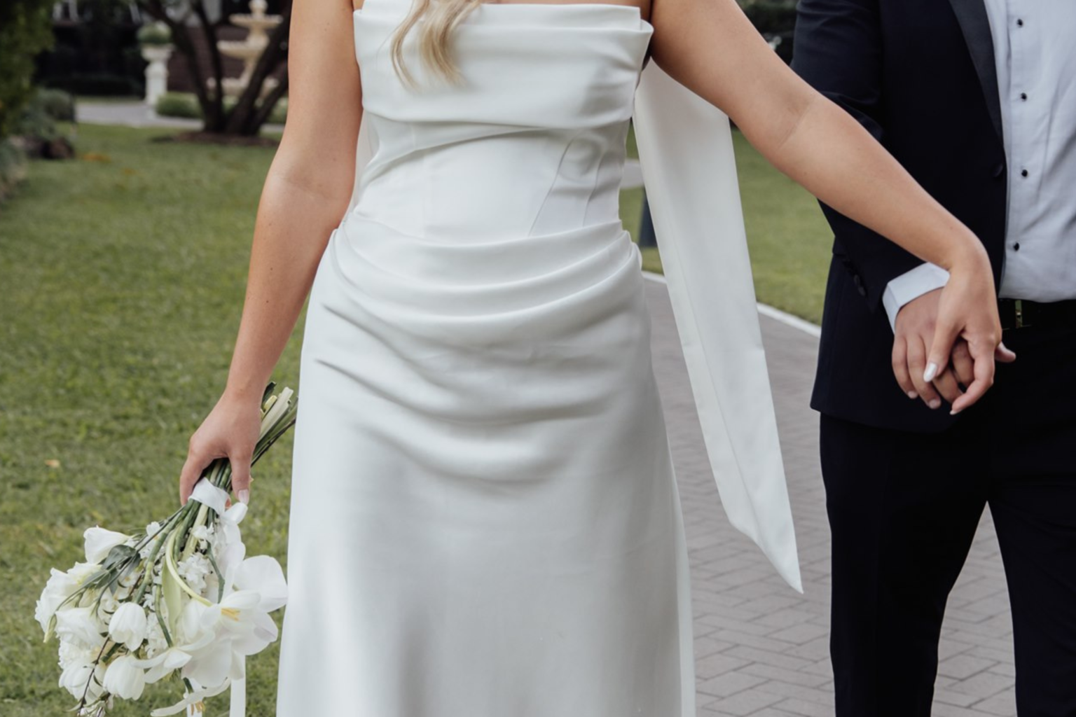 Close-up of the bride in a satin gown holding the groom's hand