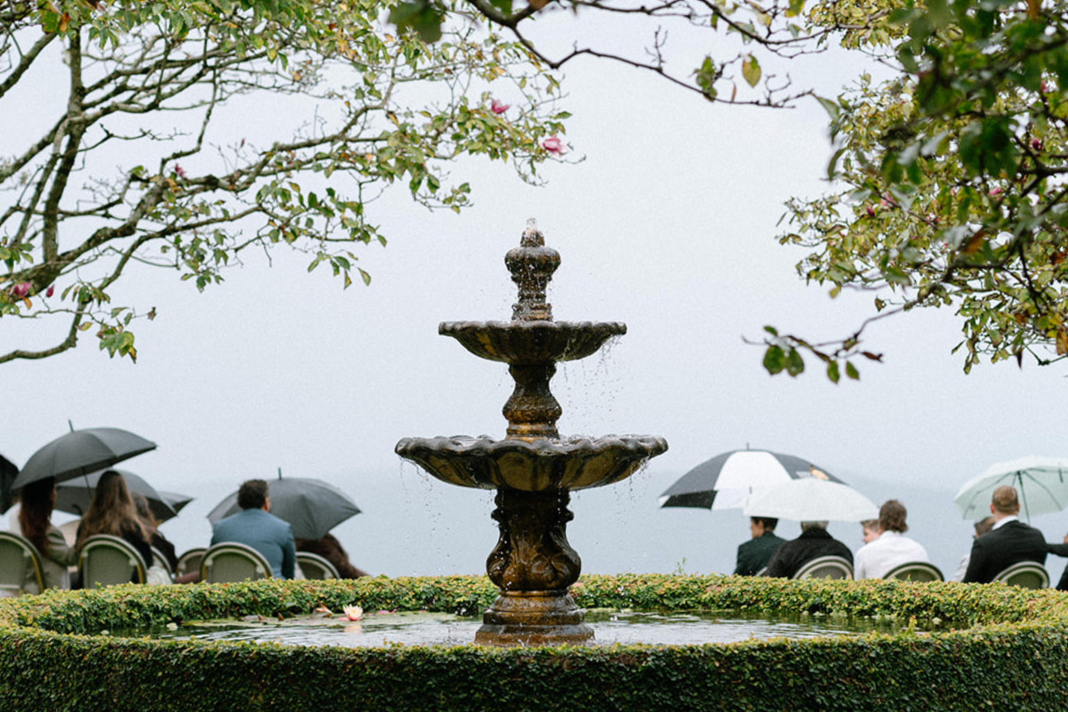 Guests with umbrellas around the fountain on a misty day