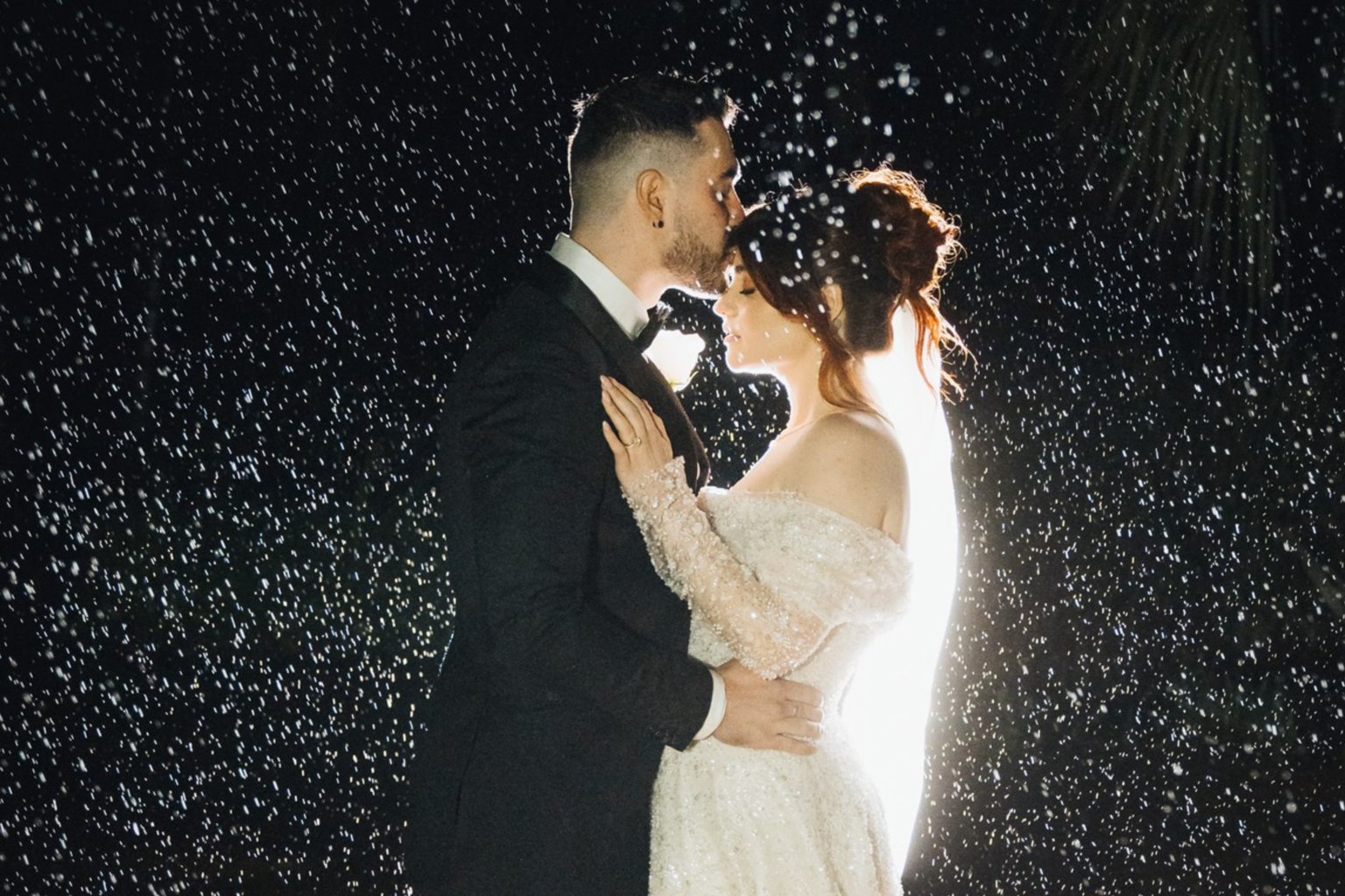Couple embracing in the rain at night, backlit by sparkles