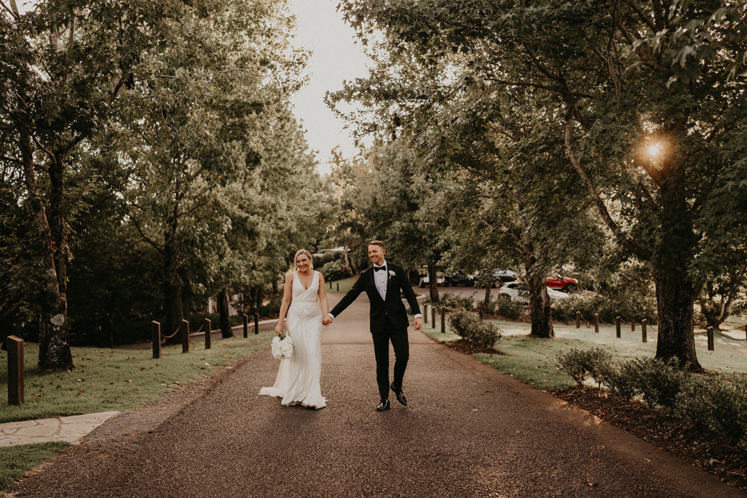Couple walking hand in hand down the tree-lined drive