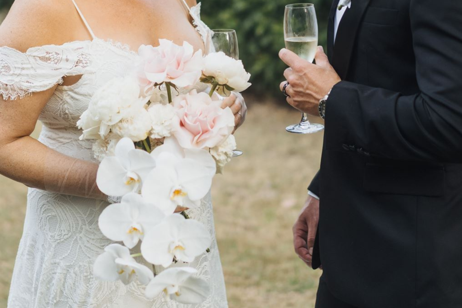 Bride holding pink and white orchids as the couple share champagne