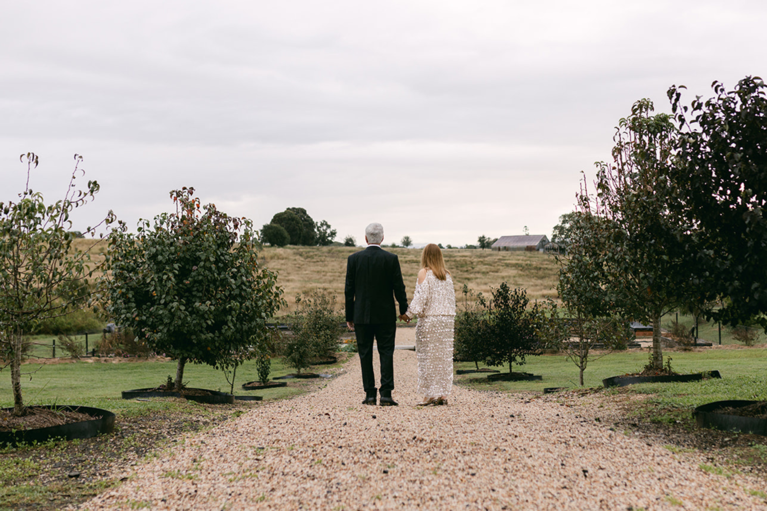 Couple walking hand in hand down the tree-lined drive at Twigley Farm
